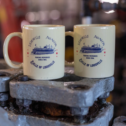 Two cream colored coffee mugs with navy text and red stars: "Idlewild, Avalon, Belle of Louisville" in circle around image of the Belle with the phrase "Making memories since 1914" underneath